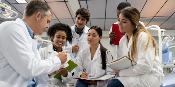 A group of students learning dental treatment from a senior dentist with note and pen in hands at a hospital alike lab.