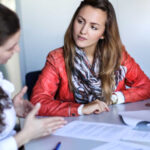 Two women in a conversation. One of them is explaining something to the other from a paper in front of them.