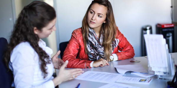 Two women in a conversation. One of them is explaining something to the other from a paper in front of them.